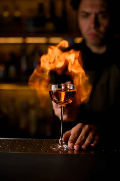 Бокал вина с напитками стоит на барной стойке и огненное пламя на заднем плане — стоковое фото