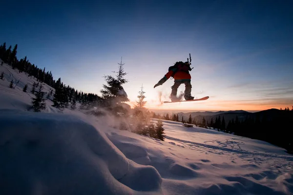 Freerider habilmente fazendo salto sobre encosta coberta de neve em snowboard contra o céu claro bonito. — Fotografia de Stock