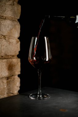 Koyu arkaplanda kırmızı şarapla dolu boş bir bardak.
