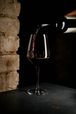 Kırmızı şarap bardağın kenarlarından süzülüp onu dolduruyor.