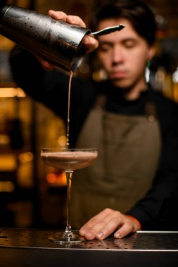 Genç barmen profesyonelce karıştırıcıdan bardağa kahverengi kokteyl dolduruyor.