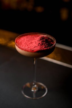 Koyu bar tezgahında kırmızı çıtırlarla süslenmiş kahverengi kokteyl.