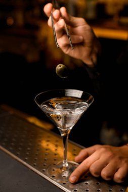 Barmen martini bardağına zeytin koymak için cımbız kullanıyor.