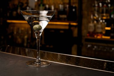 Martini bardağına zeytin katılmış berrak bir kokteylin ön fotoğrafı.