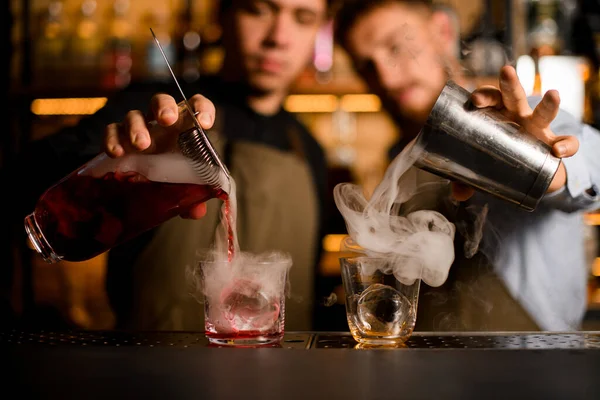 Due bicchieri poggiano sul bancone e due baristi li riempiono di fumo e alcol — Foto Stock