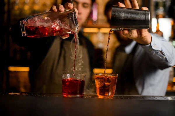 Два бармена наполняют бокалы до верха из шейкера и кувшина — стоковое фото