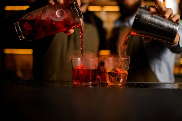 Два бармена наливают красные и коричневые алкогольные напитки из шейкера и кувшина — стоковое фото
