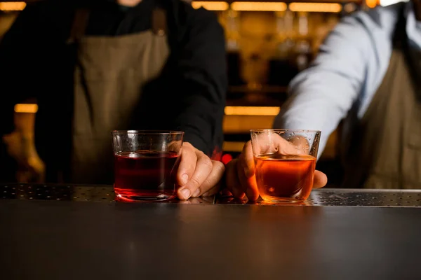 두 개의 술잔을 들고 있는 두 명의 바텐더가 붉은 색 과 갈색의 술을 마시고 있다 — 스톡 사진