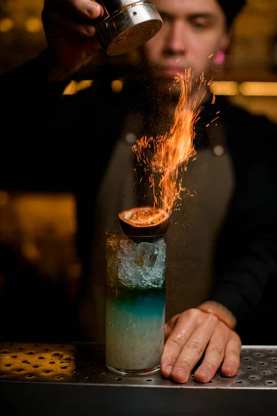 Male bartender sprinkling fired up blue alcohol drink with feijoa — Stock Photo, Image