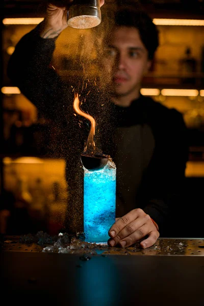 El cantinero derrama canela sobre el fuego en bebida alcohólica azul —  Fotos de Stock