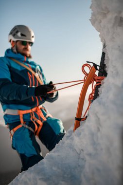 Buz baltasına odaklan. Arkadaki yamaçta ekipman ve iplerle tırmanan bir adam.