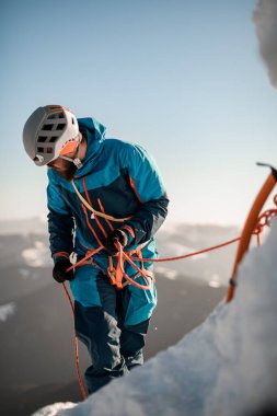 Kasklı profesyonel dağcı sigortalı. Kışın mavi gökyüzüne karşı tırmanan dağcıların işi