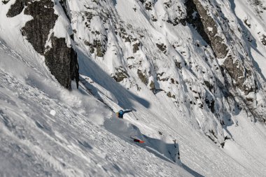 Kayalıklarla kaplı dağ yamacının güzel manzarası ve kayakçı aşağı kayıyor.