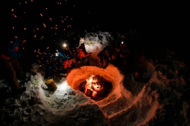 Uçan kıvılcımlarla yüksek açılı kamp ateşi manzarası ve etrafında oturup güneşlenen bir grup turist