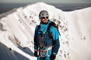 Adam karlı dağın arka planında kayak ekipmanı giyiyor.