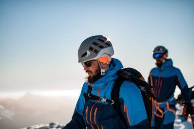 Kafasında kayak kaskı olan bir adamın mavi gökyüzü arka planına bakışı