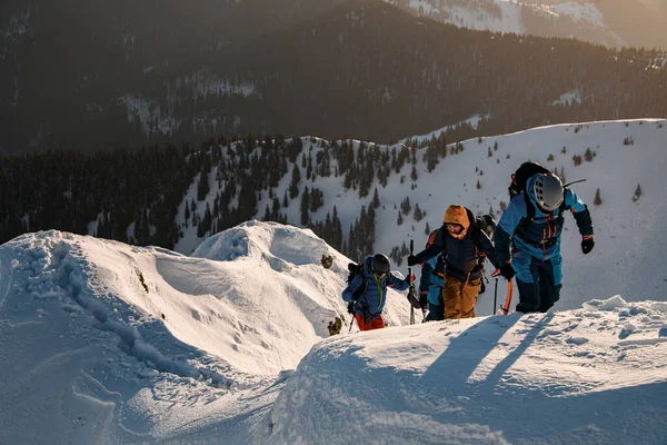 Gruppo di sciatori in tute da sci luminose che salgono sul sentiero di montagna innevato — Foto Stock