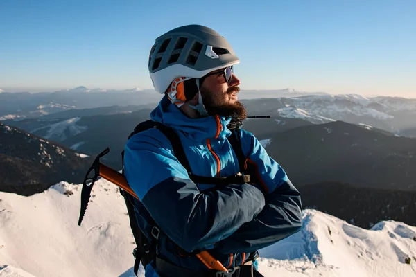 Retrato do homem no capacete e um terno de esqui com machado de gelo contra o pano de fundo da paisagem montanhosa — Fotografia de Stock