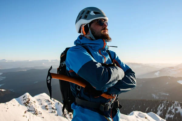 Retrato de turista masculino em capacete e um terno de esqui com machado de gelo contra o pano de fundo da paisagem de montanha de inverno — Fotografia de Stock