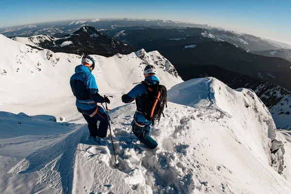 Вид сзади лыжников на вершине заснеженной горы на фоне красивого ландшафта — стоковое фото
