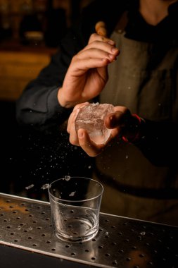 Barmenin elindeki buz parçasının yakın plan görüntüsü. Parçalarını buz kıracağıyla kırıyor.