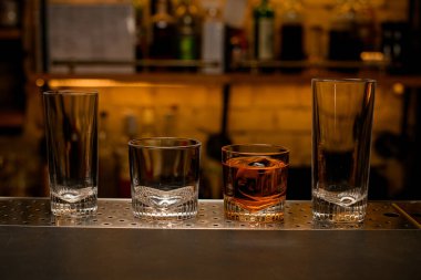 Bar tezgahında boş bir grup ve dolu bir kokteyl bardağı..
