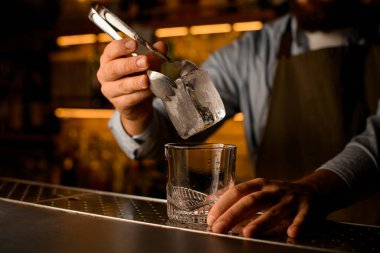 Camın üzerinde maşayla erkek eli tarafından tutulan kare buz parçasının yakın plan görüntüsü