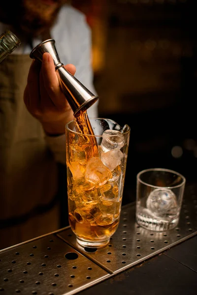 Mano del camarero vierte hábilmente la bebida de jigger en la taza de mezcla con hielo —  Fotos de Stock