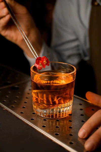 Старомодный стакан холодного напитка в баре и бармен украшая его цветами — стоковое фото