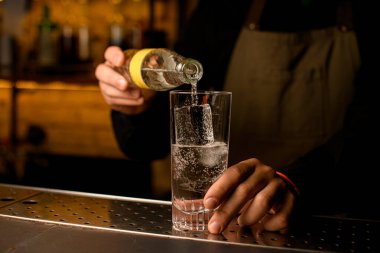 Barmenin şişeden su içtiği soğuk içecek ve buzlu bardağın önü.