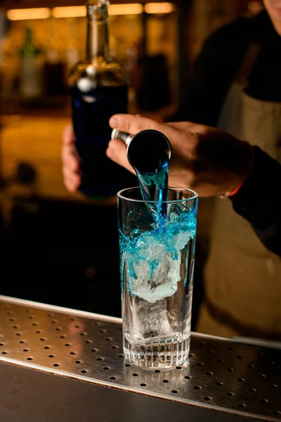 Рука бармена умело наливает синий напиток из стакана в стаканчик со льдом — стоковое фото