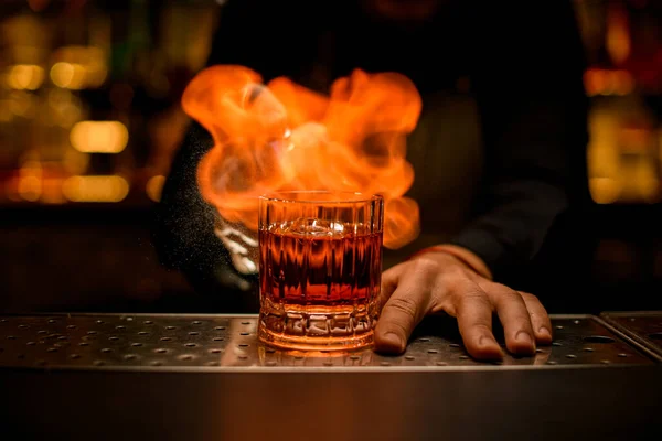 Вид спереди старомодного стакана с холодным алкогольным напитком на баре и огненным пламенем на нем — стоковое фото