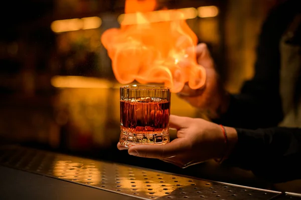 Beautiful view on old-fashioned glass with cold alcoholic drink on male hand and fire flame at background — Stock Photo, Image