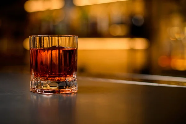 Primer plano de vidrio anticuado con bebida alcohólica y trozo de hielo sobre fondo borroso —  Fotos de Stock