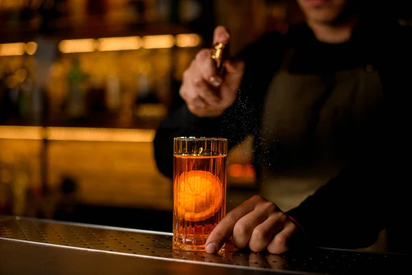 Χέρι του άνδρα μπάρμαν κρατά ένα ποτήρι κρύο αλκοολούχο ποτό με φέτα πορτοκάλι και απαλά πασπαλίζουμε σε αυτό — Φωτογραφία Αρχείου