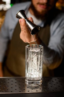 Barmenin eli jigger 'ı tutuyor ve nazikçe buzla bardağa su dolduruyor.