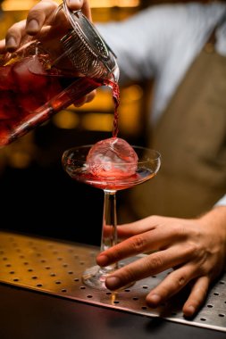 Süzgeçten filtrelenmiş karıştırma kabının buzuyla bardağa dökülen parlak bir kokteyl.