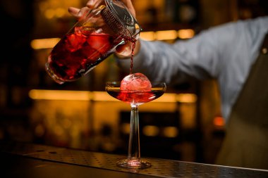 Barmenin süzgeçten filtrelenmiş bardaktan kokteyl döktüğü buzlu şarap bardağının güzel manzarası.