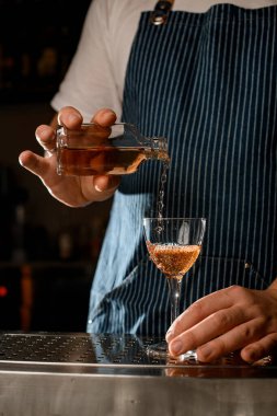 Adamın eli alkollü bir içecekle şişeyi tutuyor ve şarap bardağına döküyor.