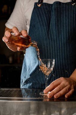 Erkek barmenin eli alkollü bir içecekle şişeyi tutuyor ve şarap bardağına döküyor.