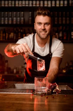 Erkek barmen, eski usul boş bir bardağın üzerinde elinde maşayla bir buz küpü tutuyor.