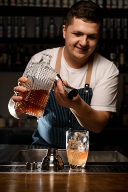 Gülümseyen erkek barmen alkollü içkiyi çelik jiggerdan karıştırıcıya döküyor.