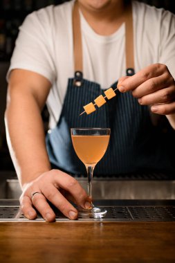 Barın tezgahında içkili kokteyl bardağı ve üstünde dekor olan barmenin eli.