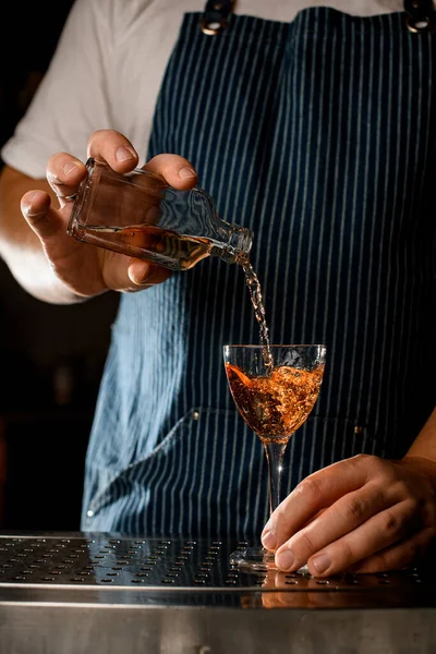 Hand bartender håller flaska med en alkoholhaltig dryck och häller i ett vinglas — Stockfoto