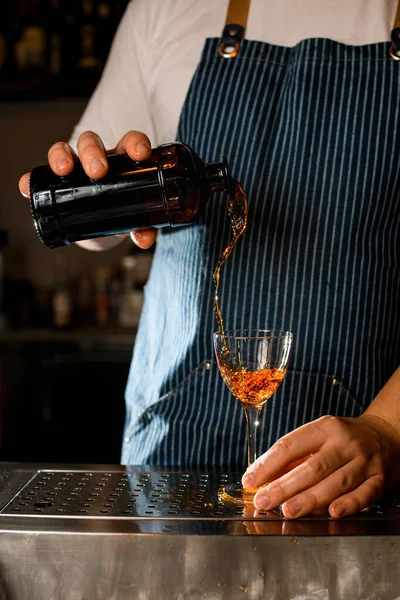 Piękny widok na strumień napoju wylewający się z butelki do kieliszka do wina na blacie baru. — Zdjęcie stockowe