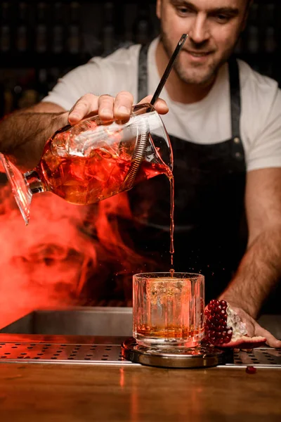 Camarero sostiene taza de mezcla con cóctel rojo y lo vierte en un vaso — Foto de Stock