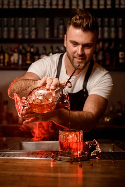 Camarero sostiene taza de mezcla con un cóctel y vierte una bebida en un vaso — Foto de Stock