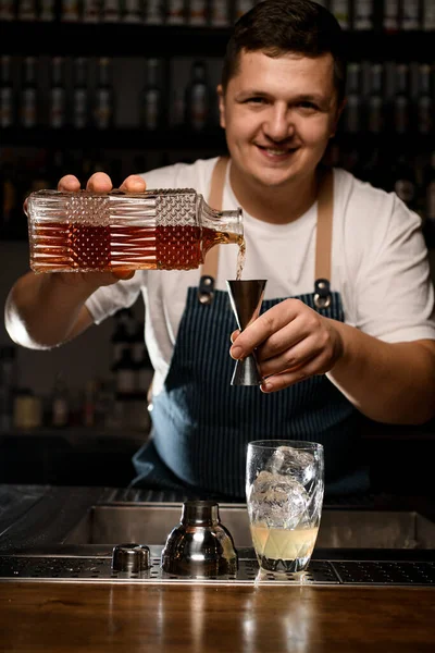Усміхнений чоловічий бармен, що наливає алкогольний напій з кристалічної пляшки в сталевий джиґер — стокове фото