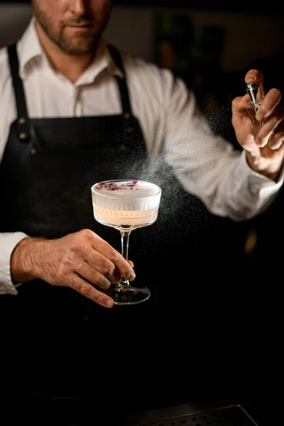 La mano di barista maschile tiene il vetro con cocktail spumeggiante saporito e spruzza su esso — Foto Stock