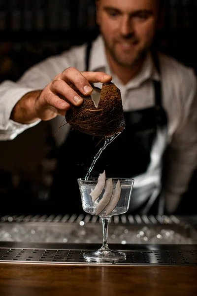 Mão do barman detém pedaço de coco e derrama leite de coco em vidro — Fotografia de Stock